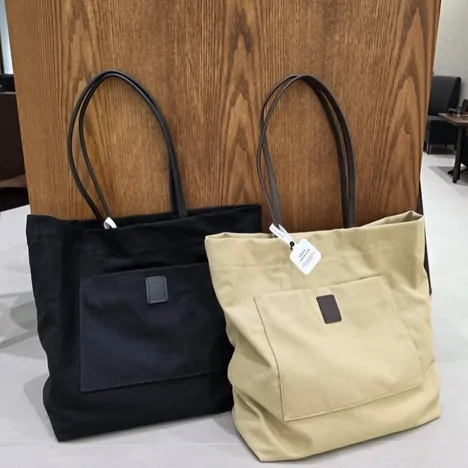 Two canvas tote bags, one black and one beige with a paper tag
