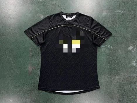 A black short-sleeve tee with a blurred chest graphic, laid flat on a green surface